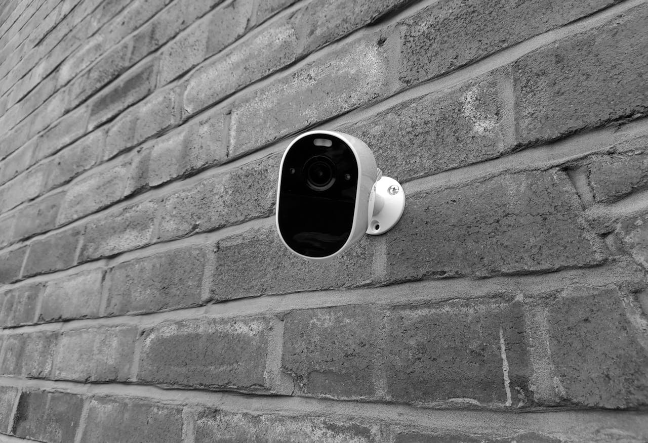 Close-up of a security camera mounted on a brick wall in monochrome.
